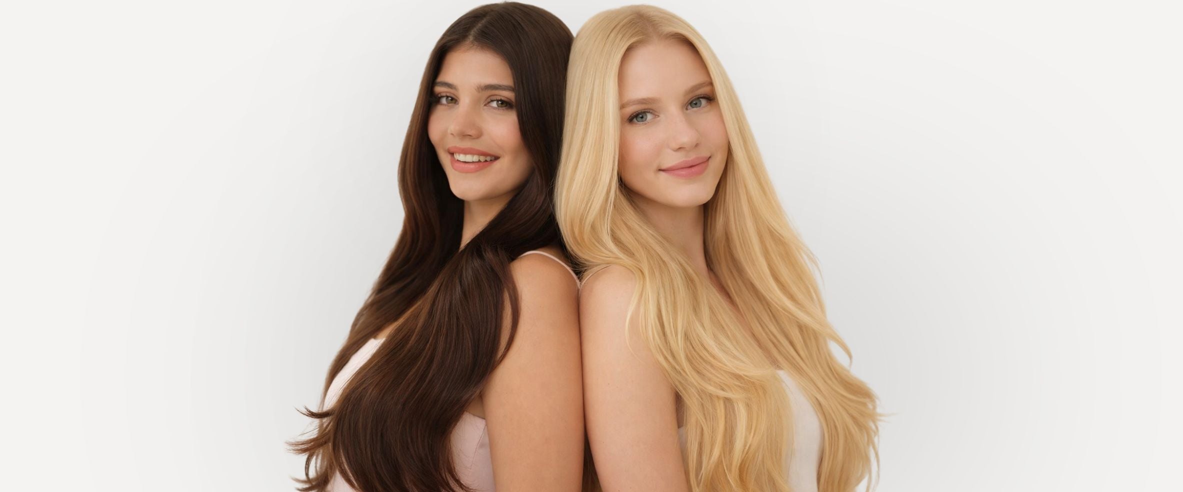 Two women with long hair, one brown and one blonde, standing back-to-back on a white background.